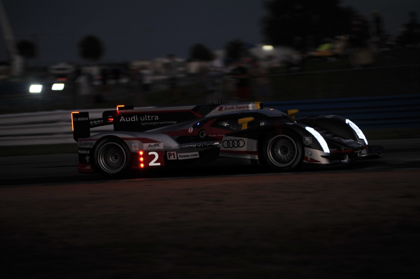 Black and red Audi R18 prototype number 2 at dusk with its headlights on
