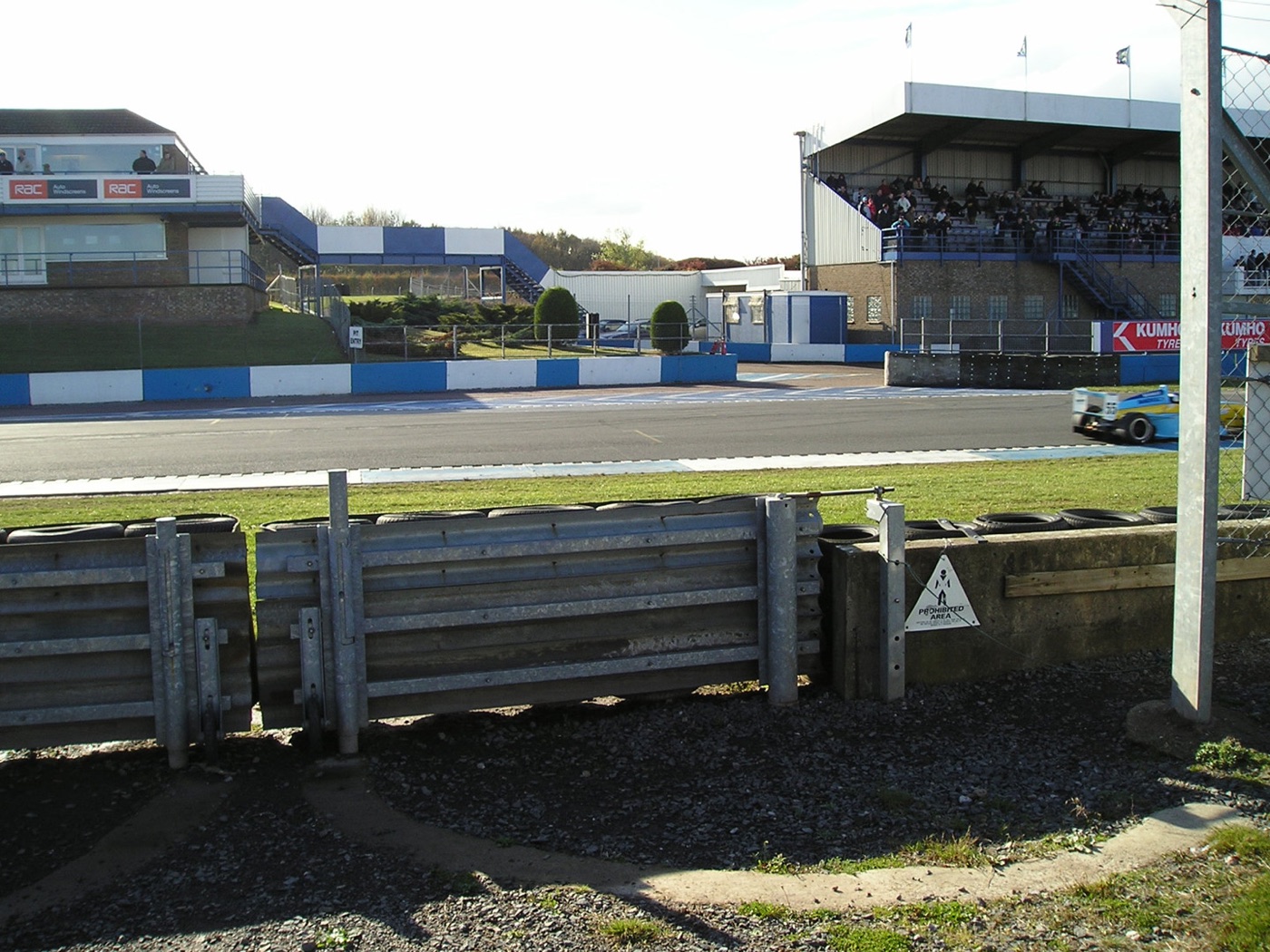 Donington Park pit lane entry with blue and white kerbs, a grandstand and race control building beyond the track
