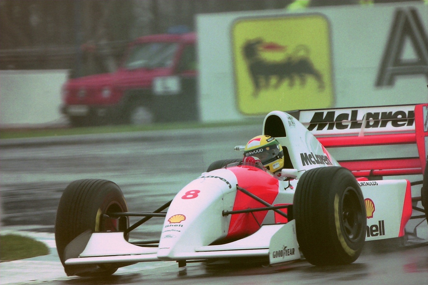 Ayrton Senna in the red and white McLaren number 8 on a wet track, spray coming off the tyres