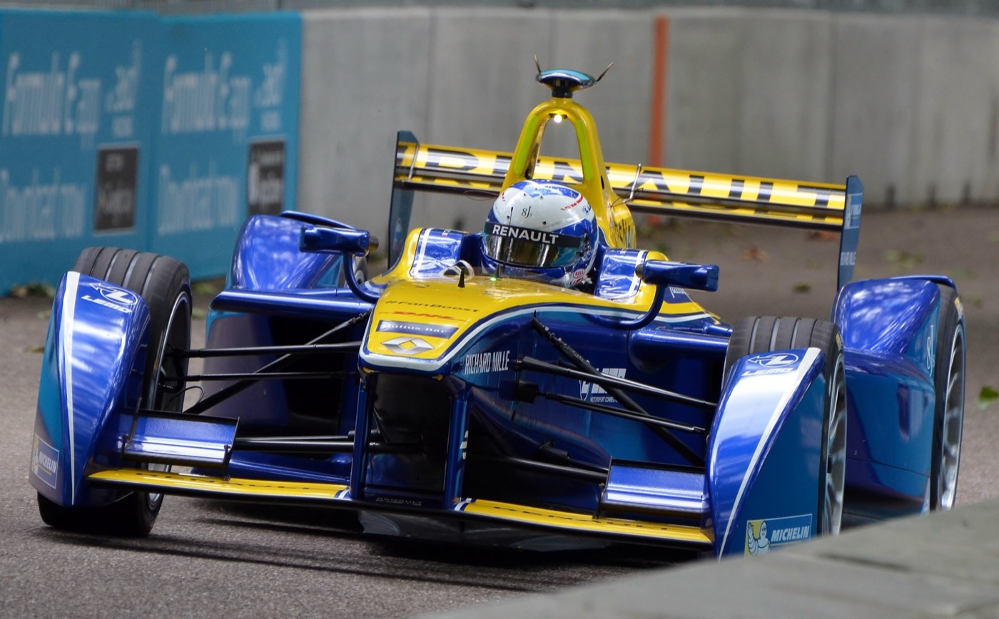 Blue and yellow Renault e.dams Formula E car with a Renault rear wing, cornering between concrete walls on a street circuit