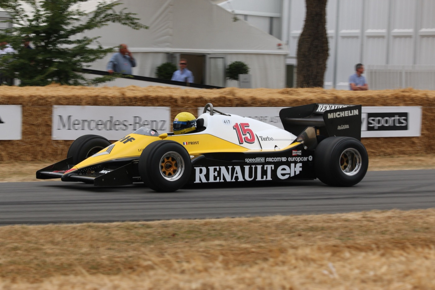 Yellow, white and black Renault RE40 turbo Formula One car, number 15, with Prost’s name on the side, driven along the straw-bale-lined hill at Goodwood