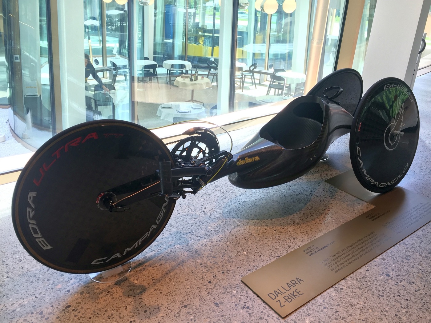 Black carbon-fibre Dallara Z-bike handbike with disc wheels on display above a plaque