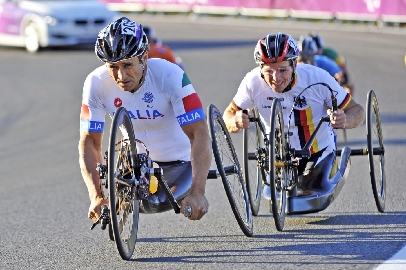 Alex Zanardi in a white Italia jersey and black helmet leading a German rider on handbikes at Brands Hatch