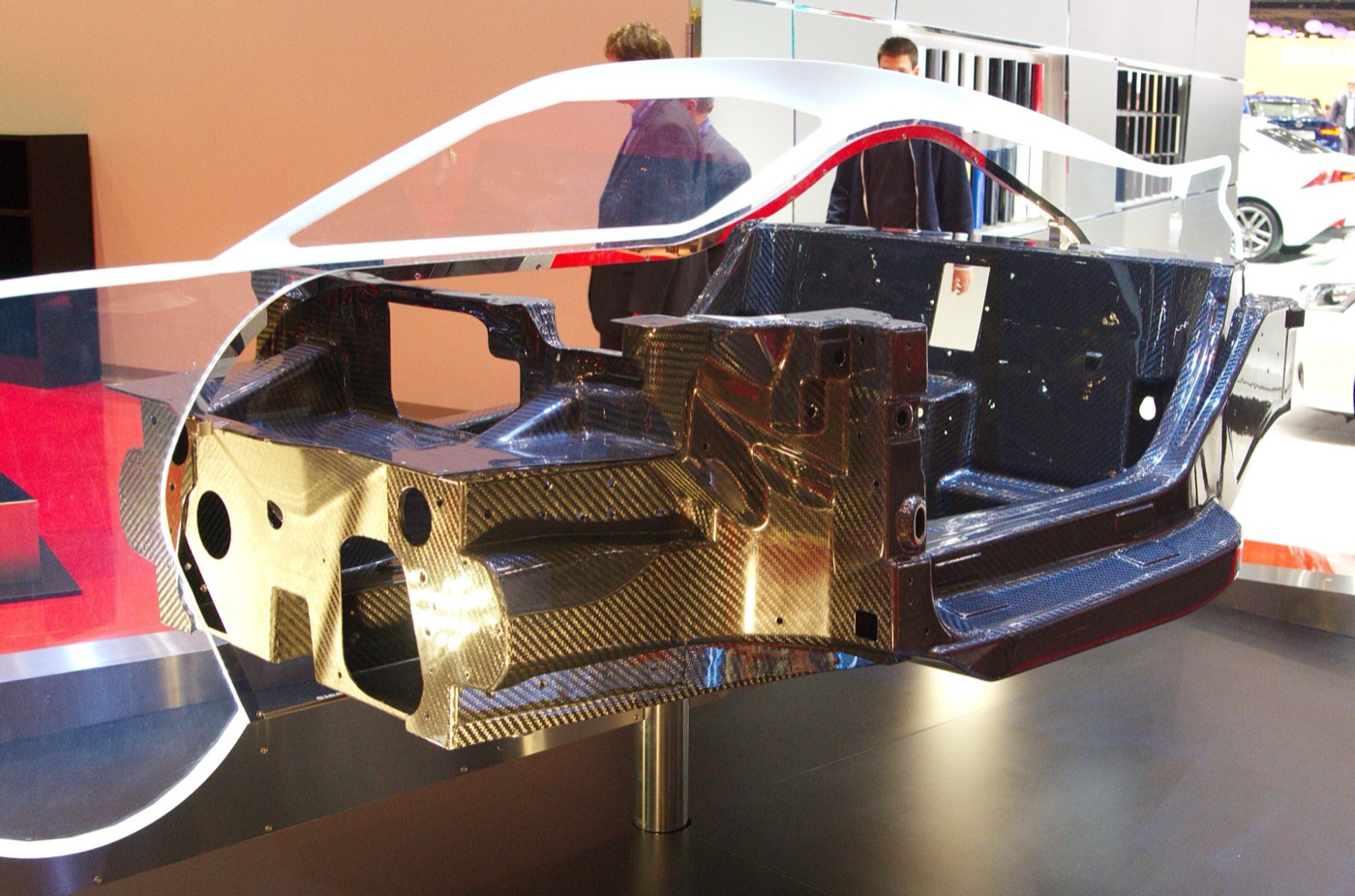Bare carbon fibre monocoque of the Alfa Romeo 4C mounted on a stand inside a clear outline of the car