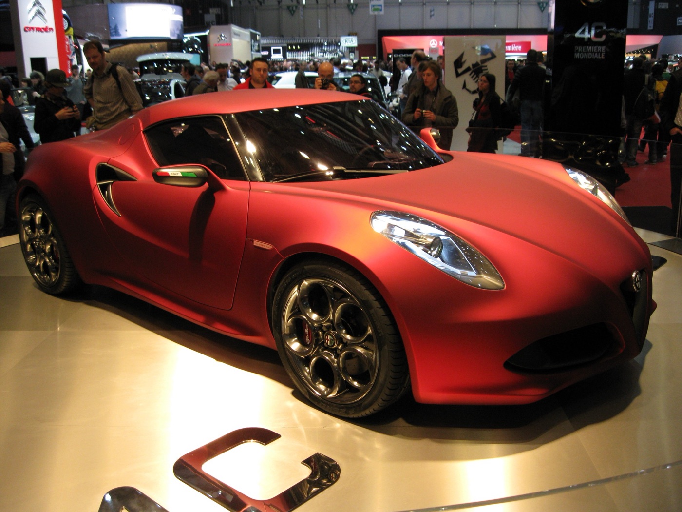 Matt red Alfa Romeo 4C Concept on a turntable at the Geneva motor show, with visitors photographing it