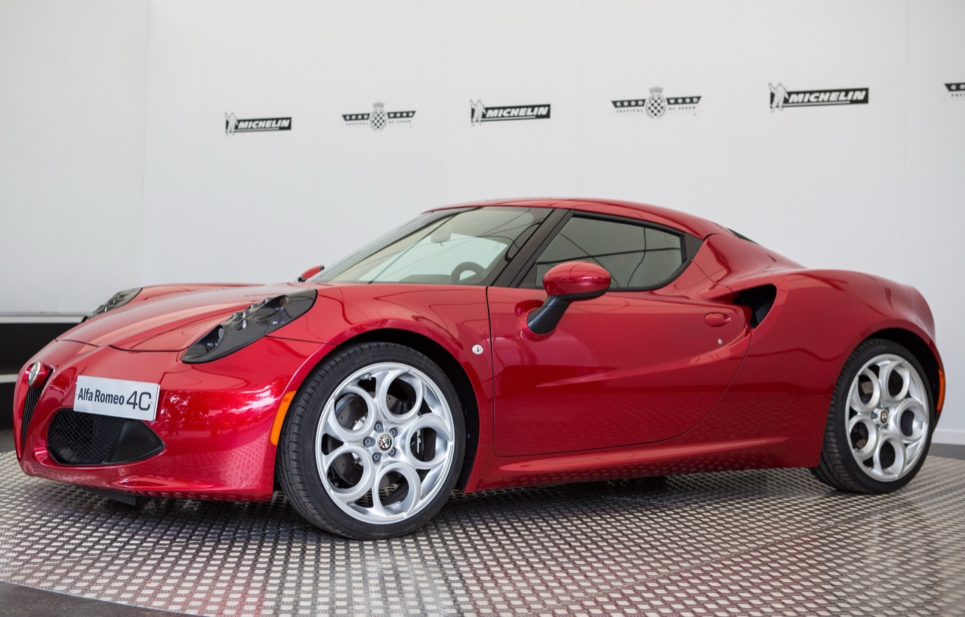 Red Alfa Romeo 4C coupé with silver five-hole wheels on a display stand in front of a white wall