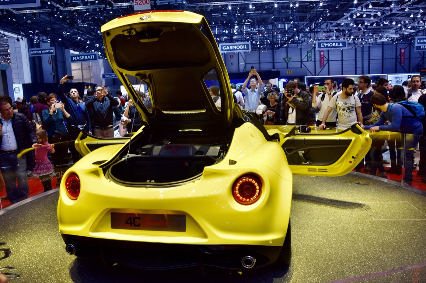 Yellow Alfa Romeo 4C Spider seen from behind with its engine cover and doors open, surrounded by show visitors