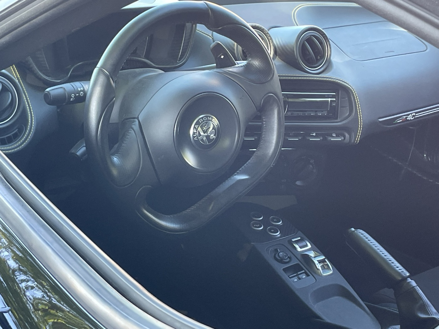Cabin of an Alfa Romeo 4C Spider showing the flat-bottomed steering wheel, paddles, small stereo and gear buttons on the centre console