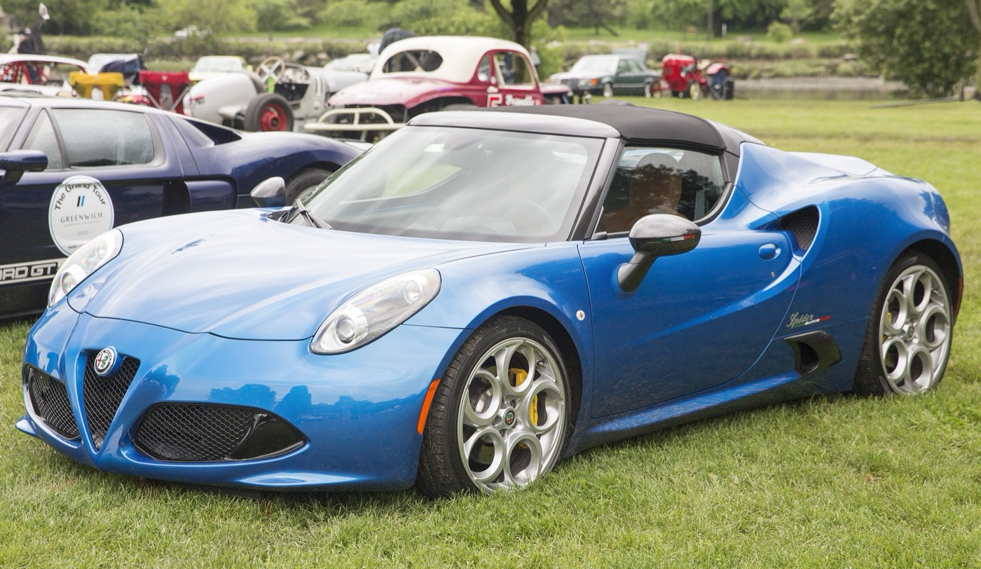 Blue Alfa Romeo 4C Spider Italia with its roof fitted, parked on grass beside other classic cars