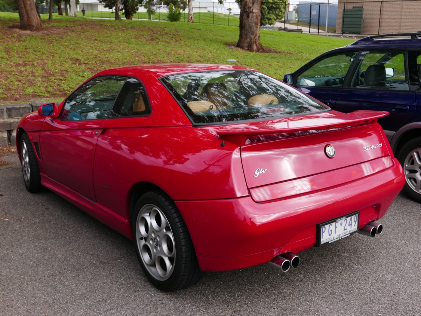 Red Alfa Romeo GTV seen from the rear three-quarter with a 3.0 V6 24V badge, a boot spoiler and twin twin-pipe exhausts