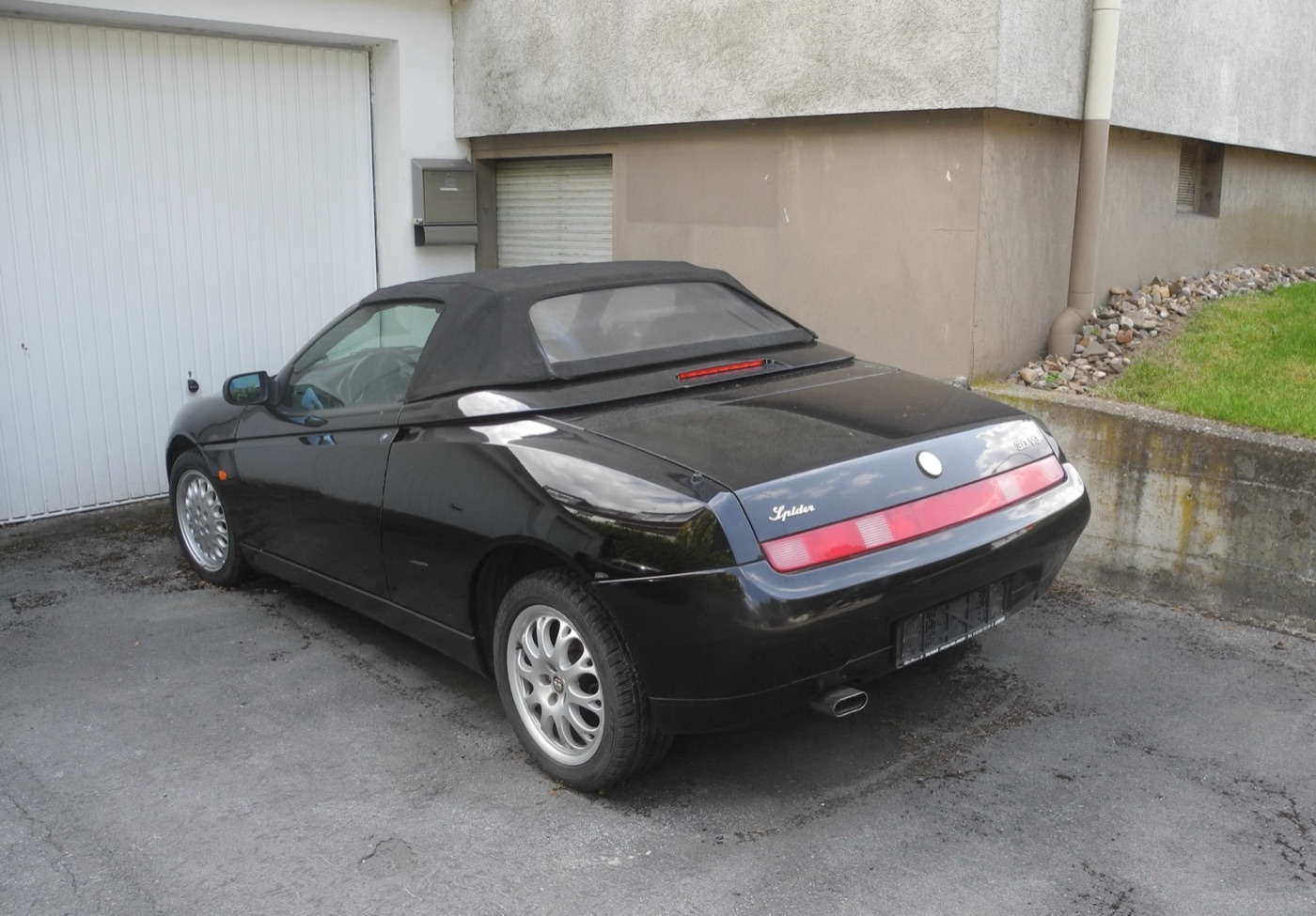Black Alfa Romeo Spider with its black cloth roof up, seen from behind, with a Spider script badge and a 3.0 V6 badge on the boot lid