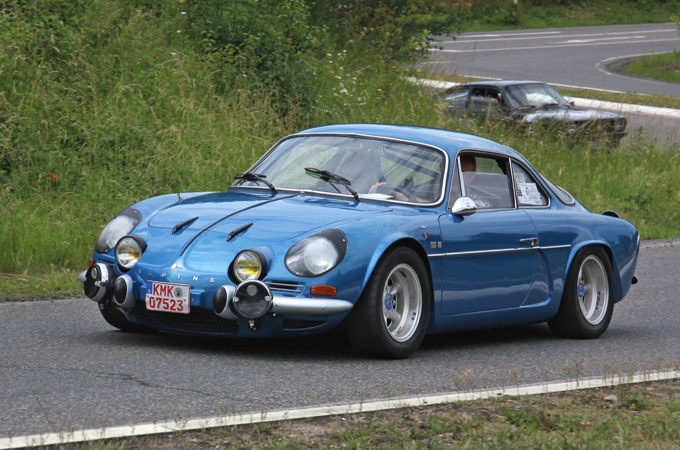 Blue Alpine A110 1300G Berlinette with four driving lamps on a country road