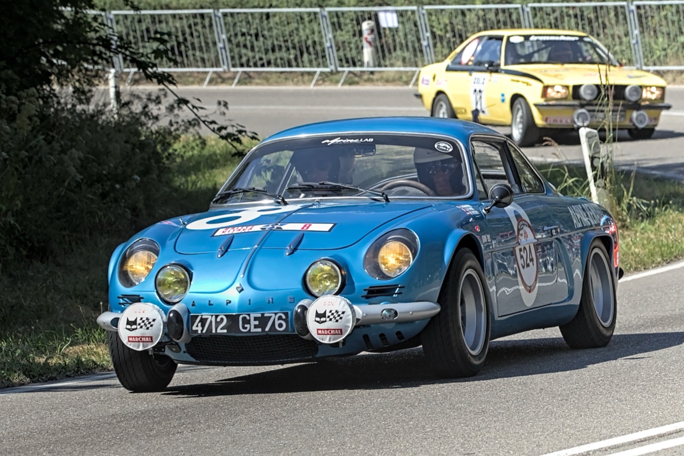 Blue 1973 Alpine A110 1800 Group 4 rally car with yellow driving lamps on a closed road