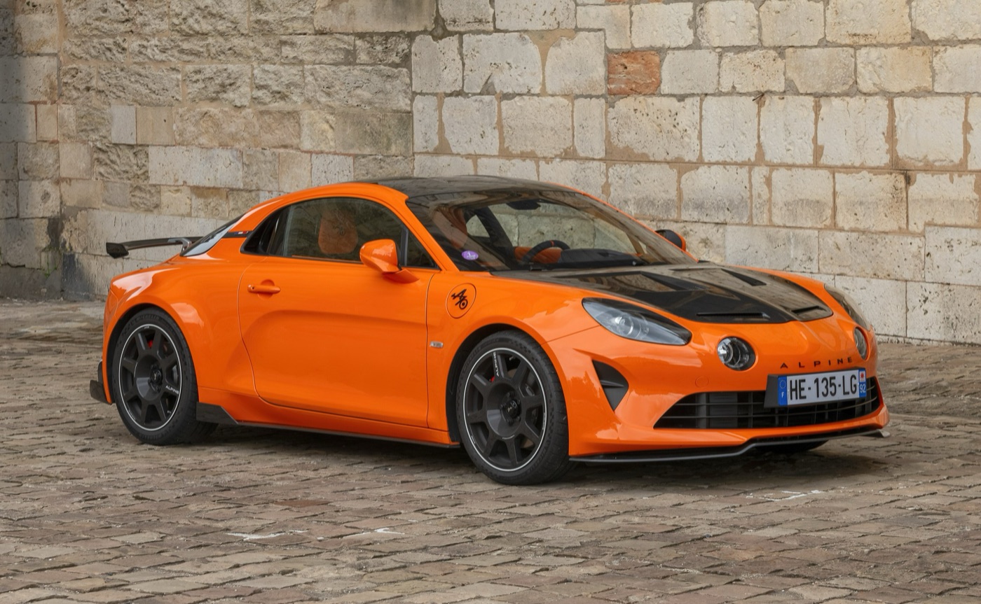 Orange Alpine A110 R Ultime with a black carbon bonnet in front of a stone wall