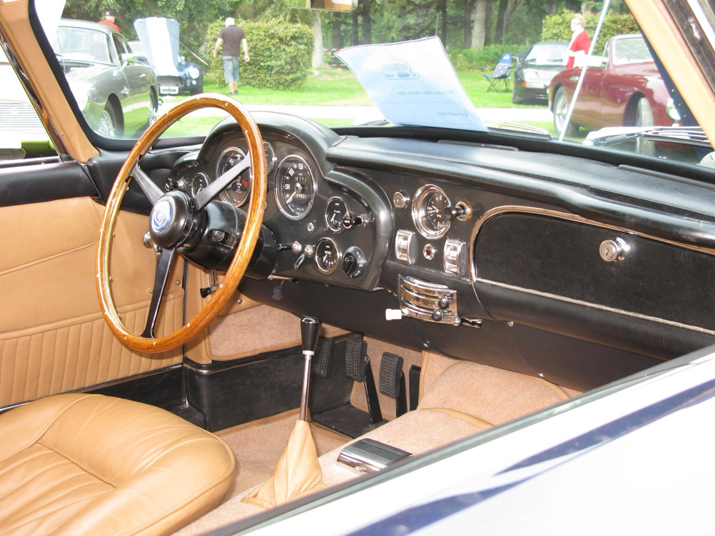 Interior of a 1965 DB5 with a wood-rimmed steering wheel, black dashboard full of round dials and tan leather seats