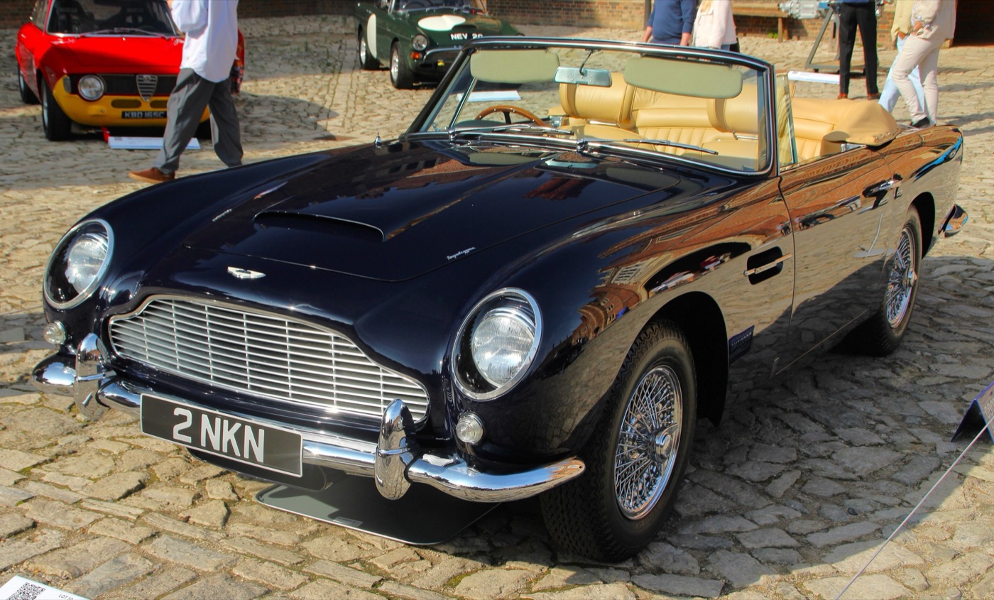 Dark blue DB5 convertible with the hood down and tan leather seats, on cobbles at a concours