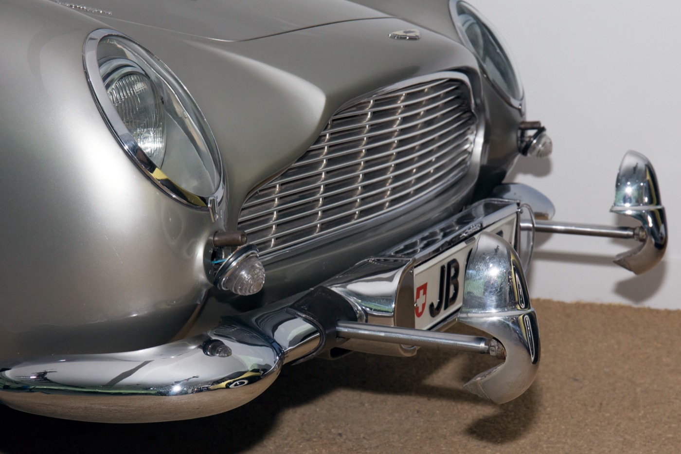 Close-up of the front of a silver DB5 with its chrome over-rider rams pushed forward on rods and a Swiss JB number plate