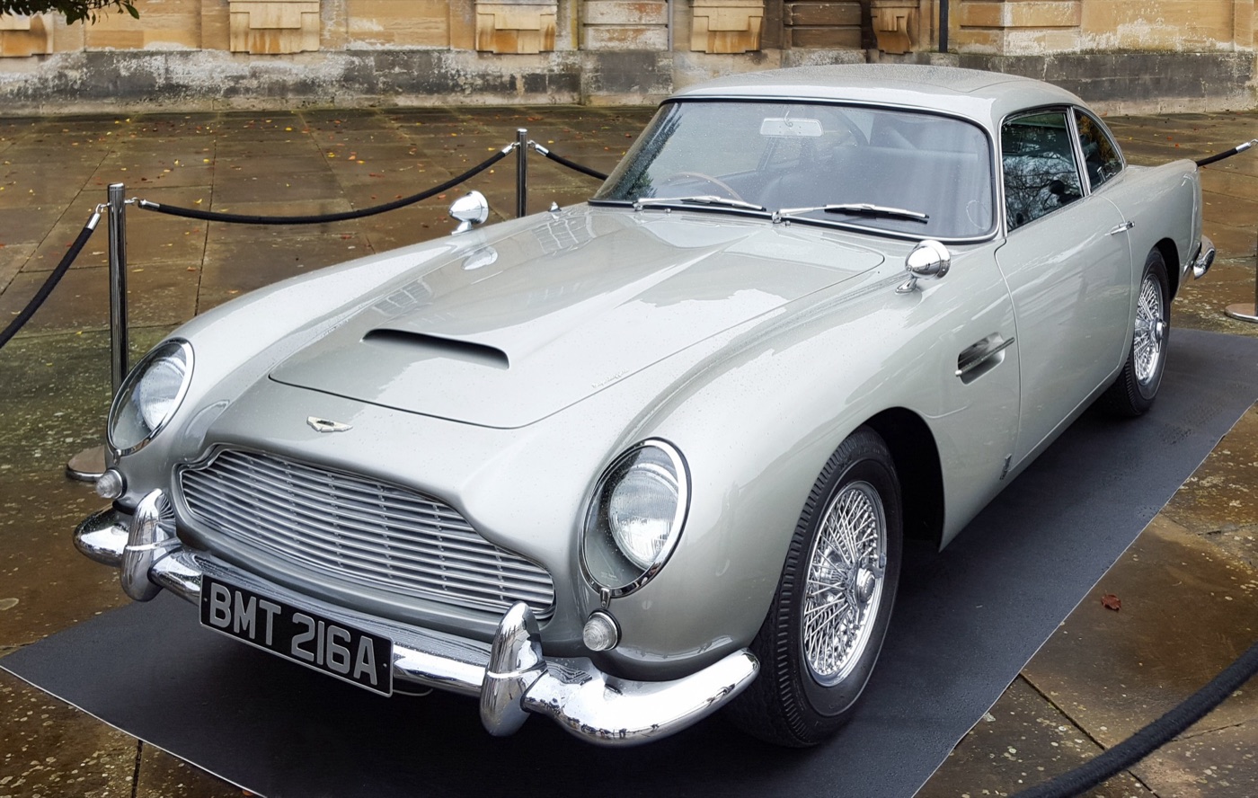Silver DB5 with the number plate BMT 216A on display behind rope barriers in a palace courtyard on a wet day