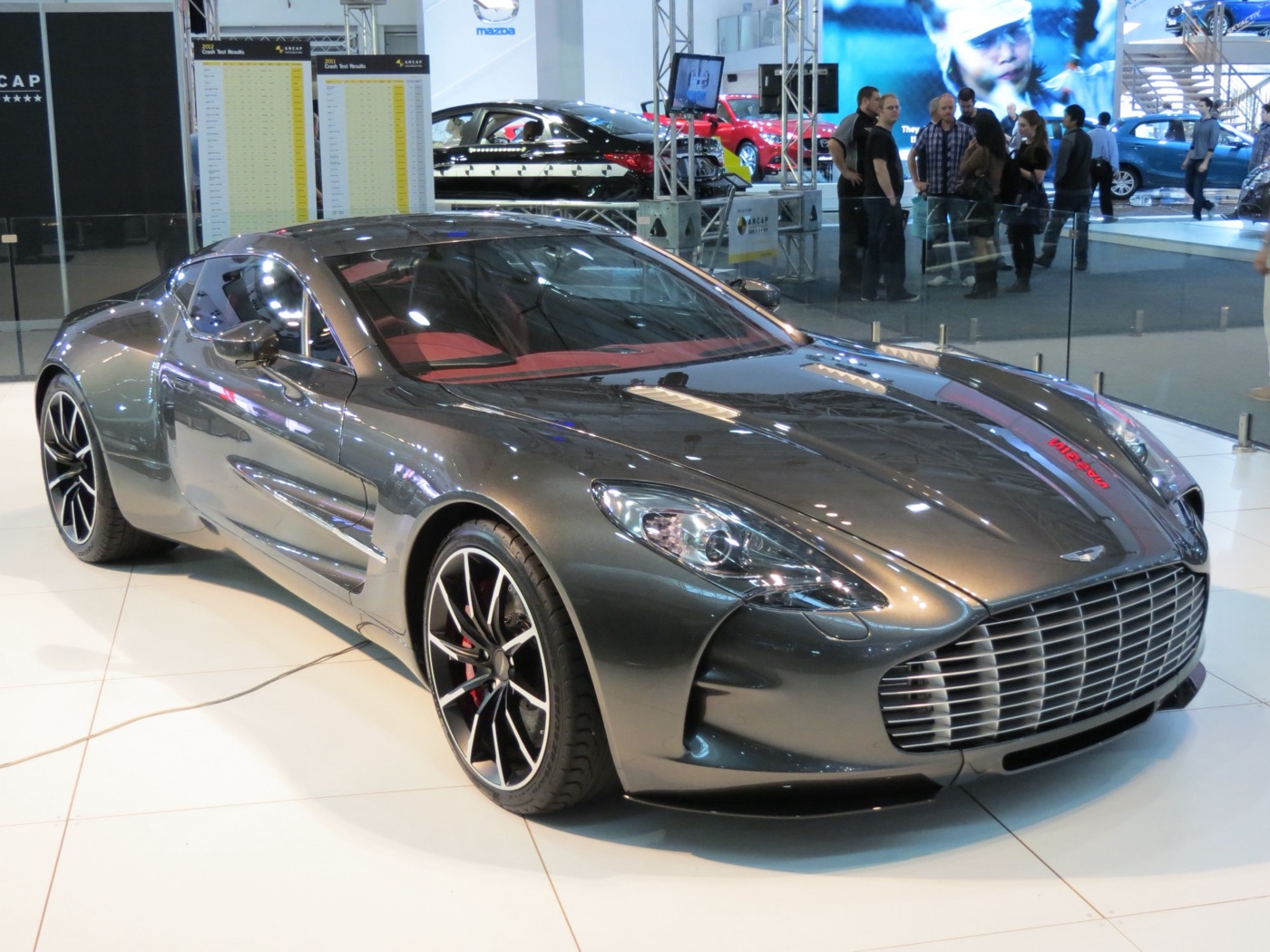 Grey Aston Martin One-77 coupé on a white stand at a motor show