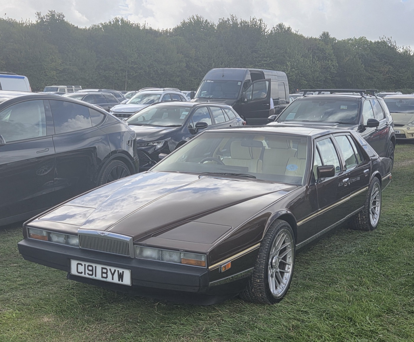 Dark brown 1986 Aston Martin Lagonda wedge-shaped saloon parked on grass among modern cars