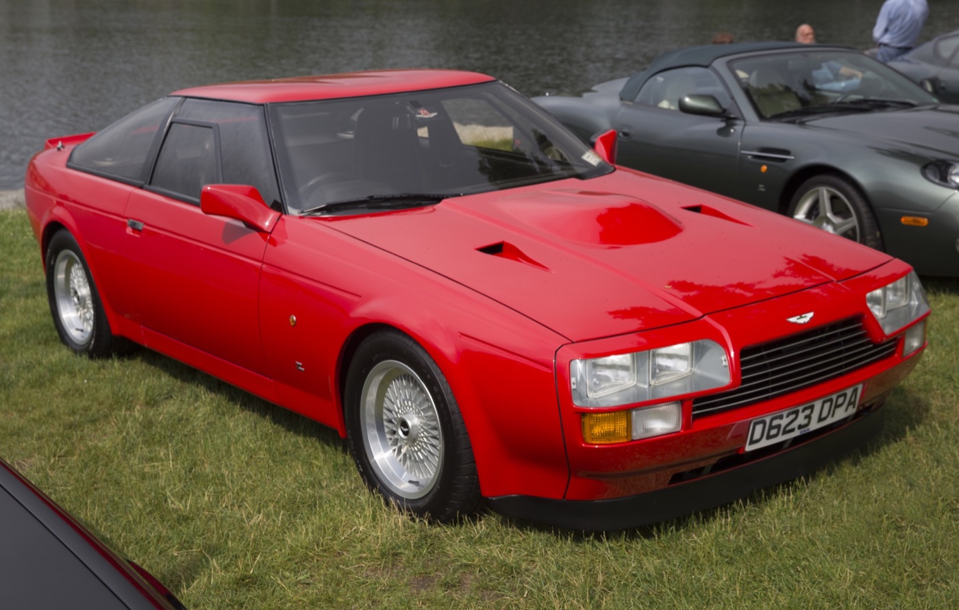 Red 1987 Aston Martin V8 Vantage Zagato coupé with a bonnet bulge, parked on grass beside a lake