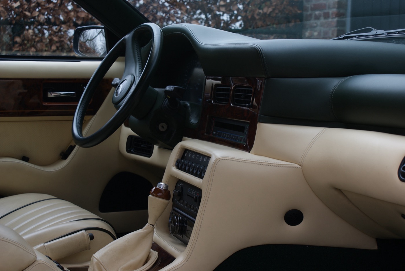 Interior of a 1991 Aston Martin Virage with cream leather, a dark green dashboard top, walnut veneer and a manual gear lever