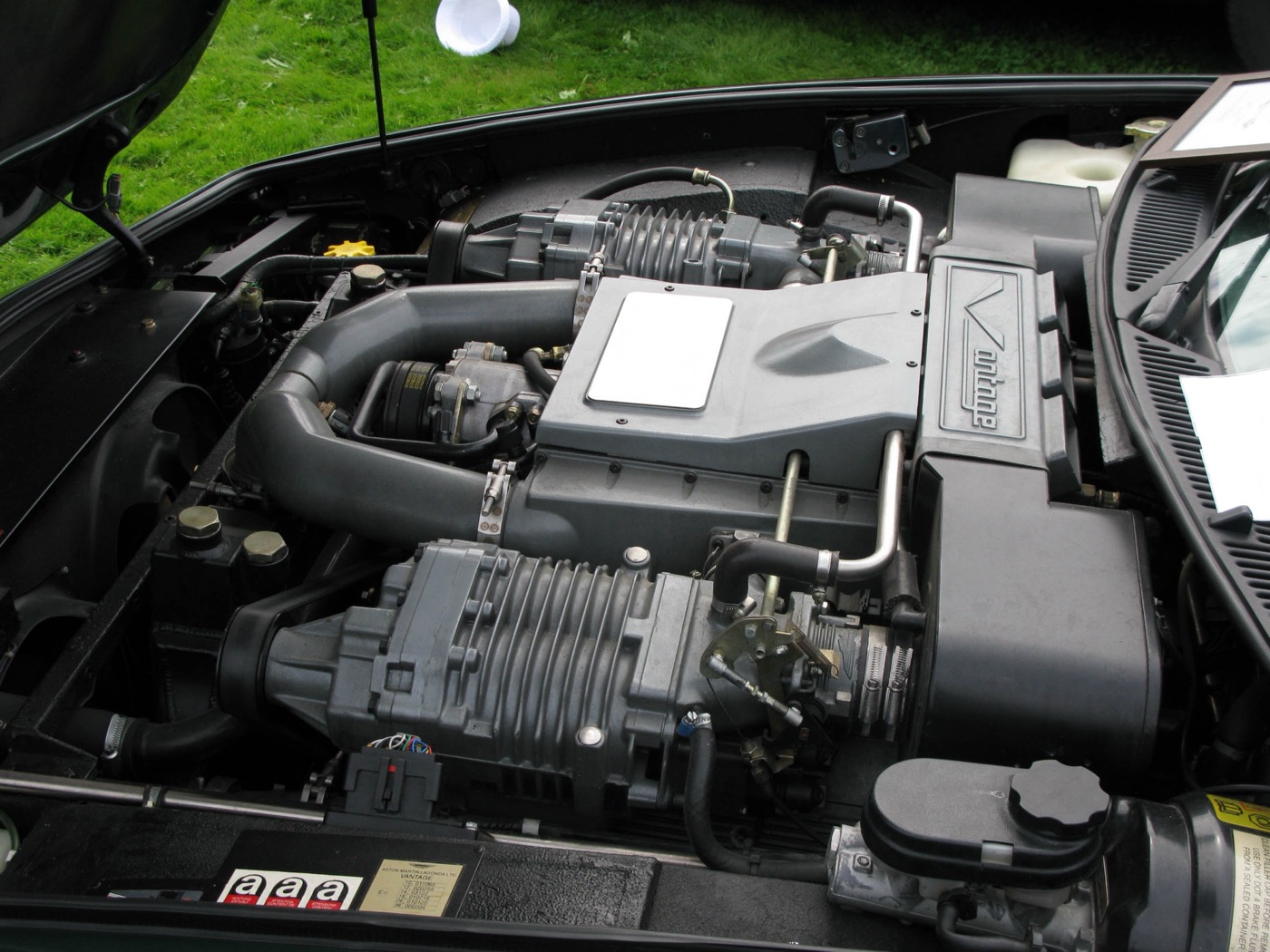 Engine bay of an Aston Martin Vantage showing the 5.3-litre V8 with its two superchargers and a Vantage-badged intake cover