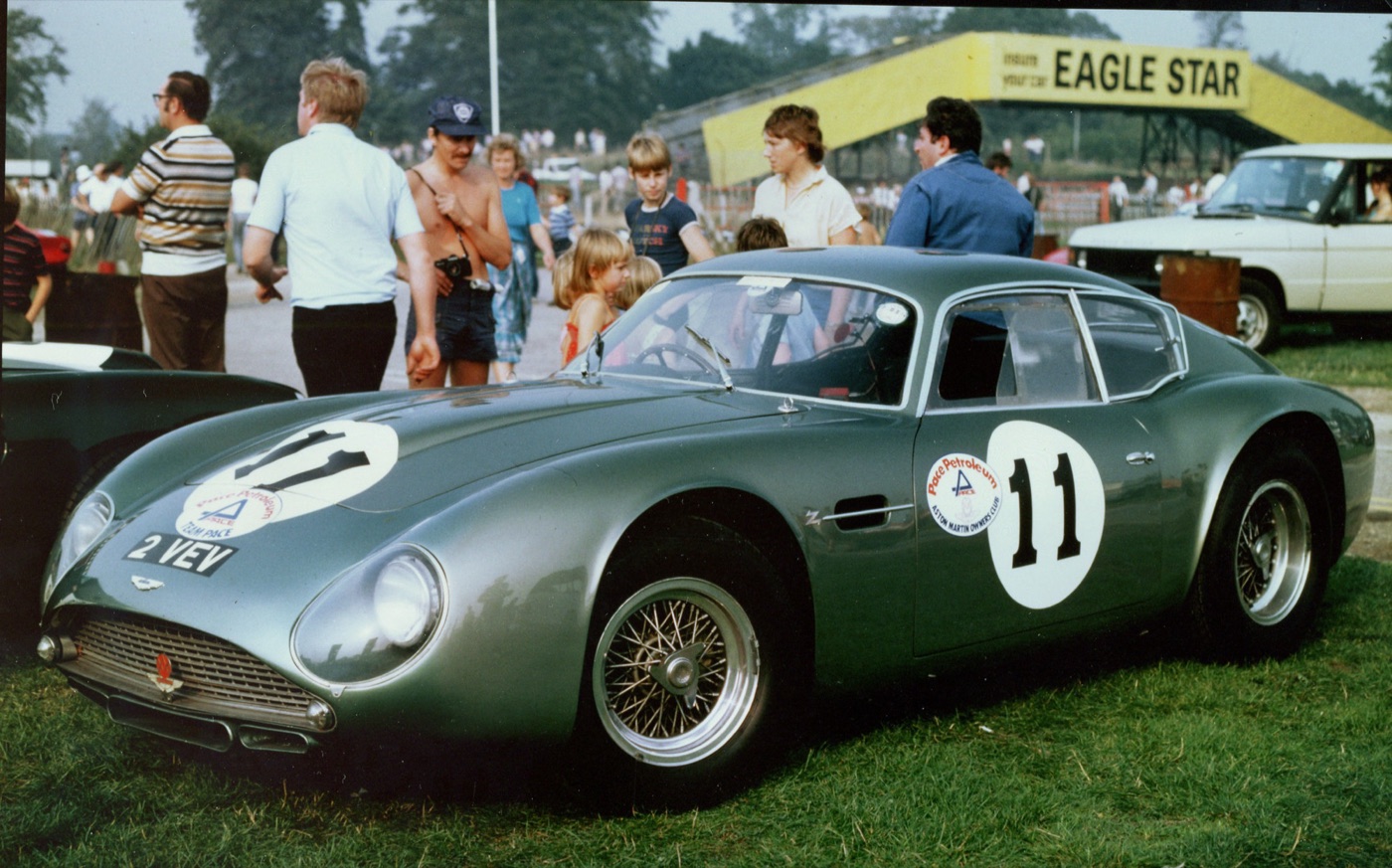 Green DB4 GT Zagato 2 VEV with racing number 11 and wire wheels parked on grass at Oulton Park, spectators behind