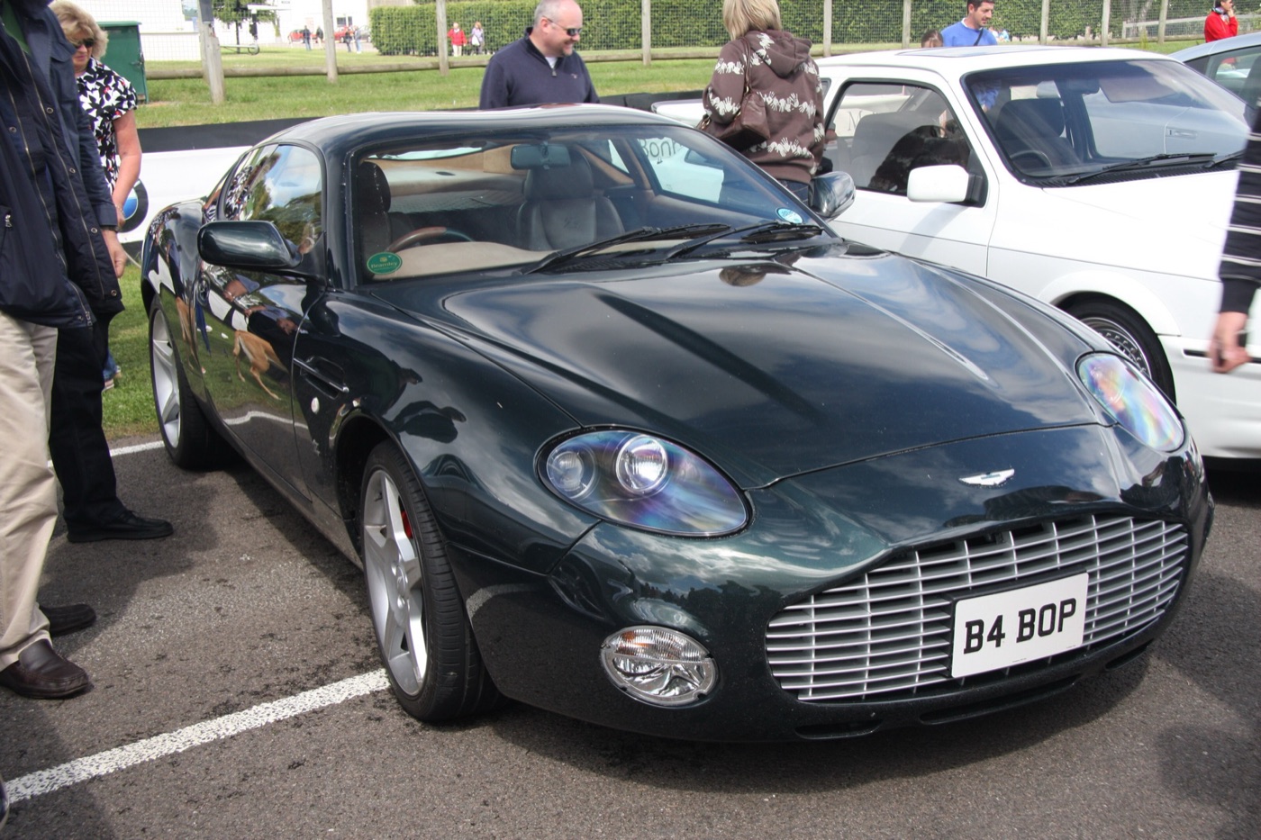 Dark green Aston Martin DB7 Zagato with a large chrome-slatted grille and round fog lamps, registration B4 BOP, parked on tarmac in a paddock