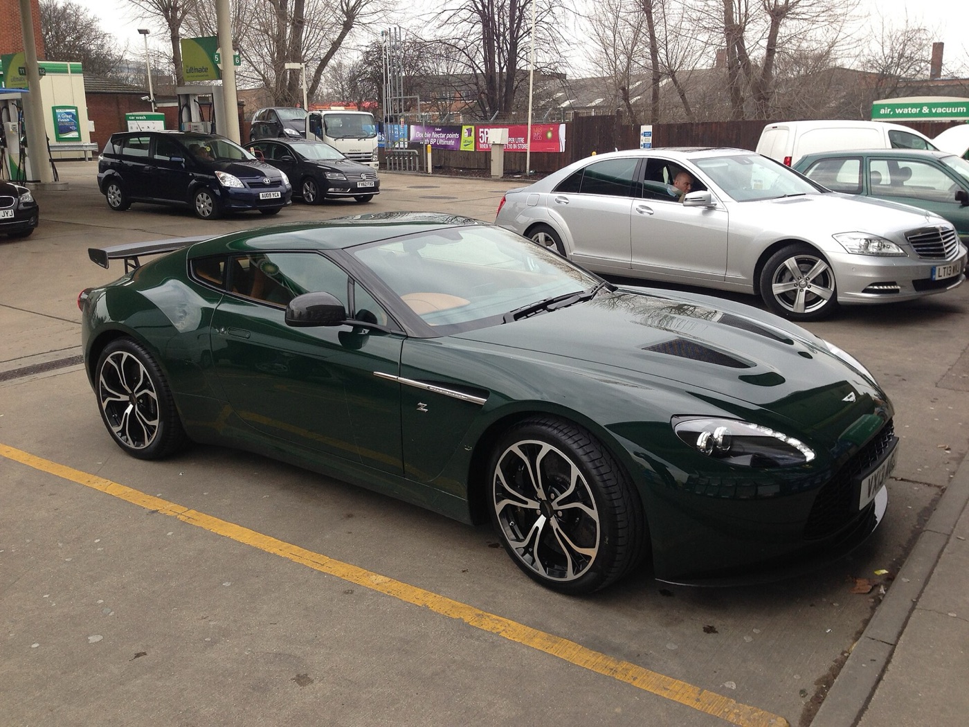Dark green Aston Martin V12 Zagato with a fixed rear wing and black wheels on a petrol-station forecourt in Park Royal, west London
