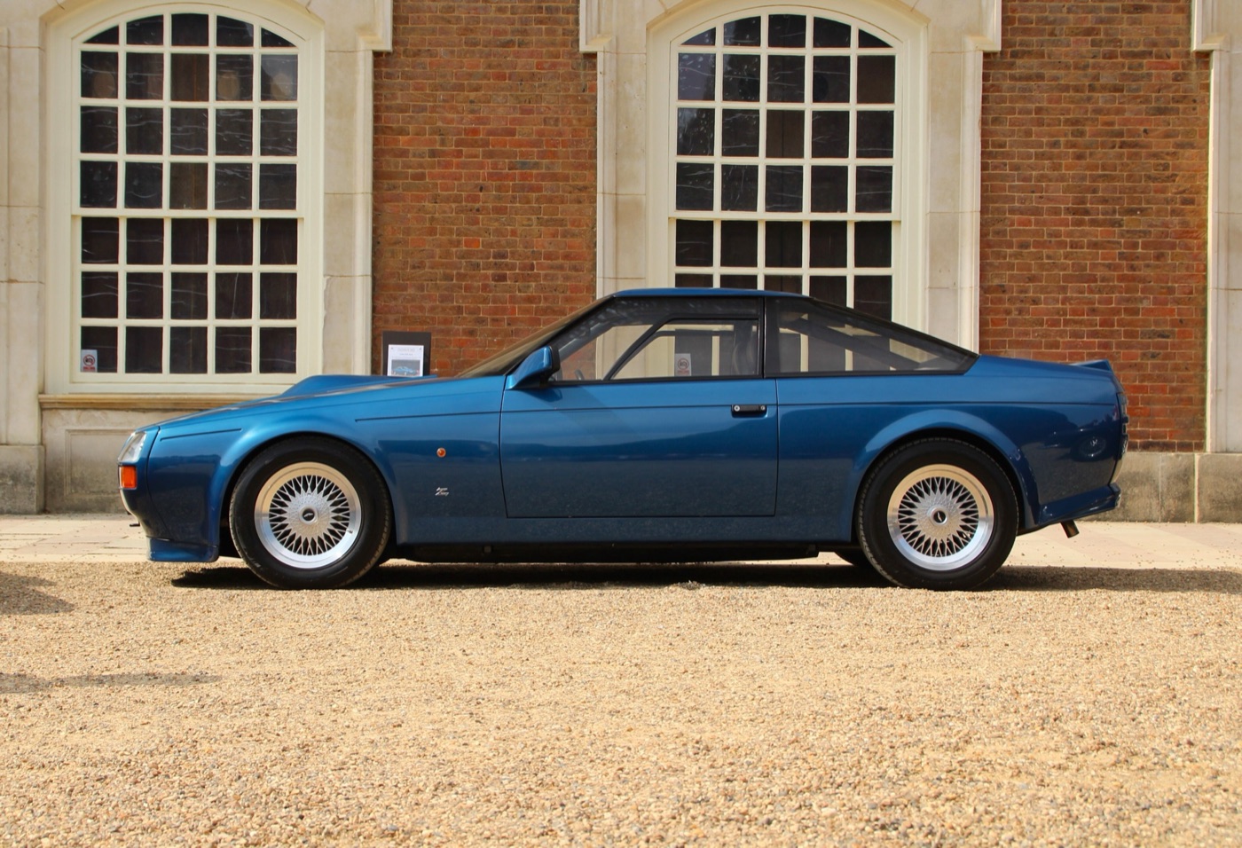 Blue 1987 Aston Martin V8 Vantage Zagato in profile with flush glazing, a short tail and multi-spoke wheels, in front of a brick building