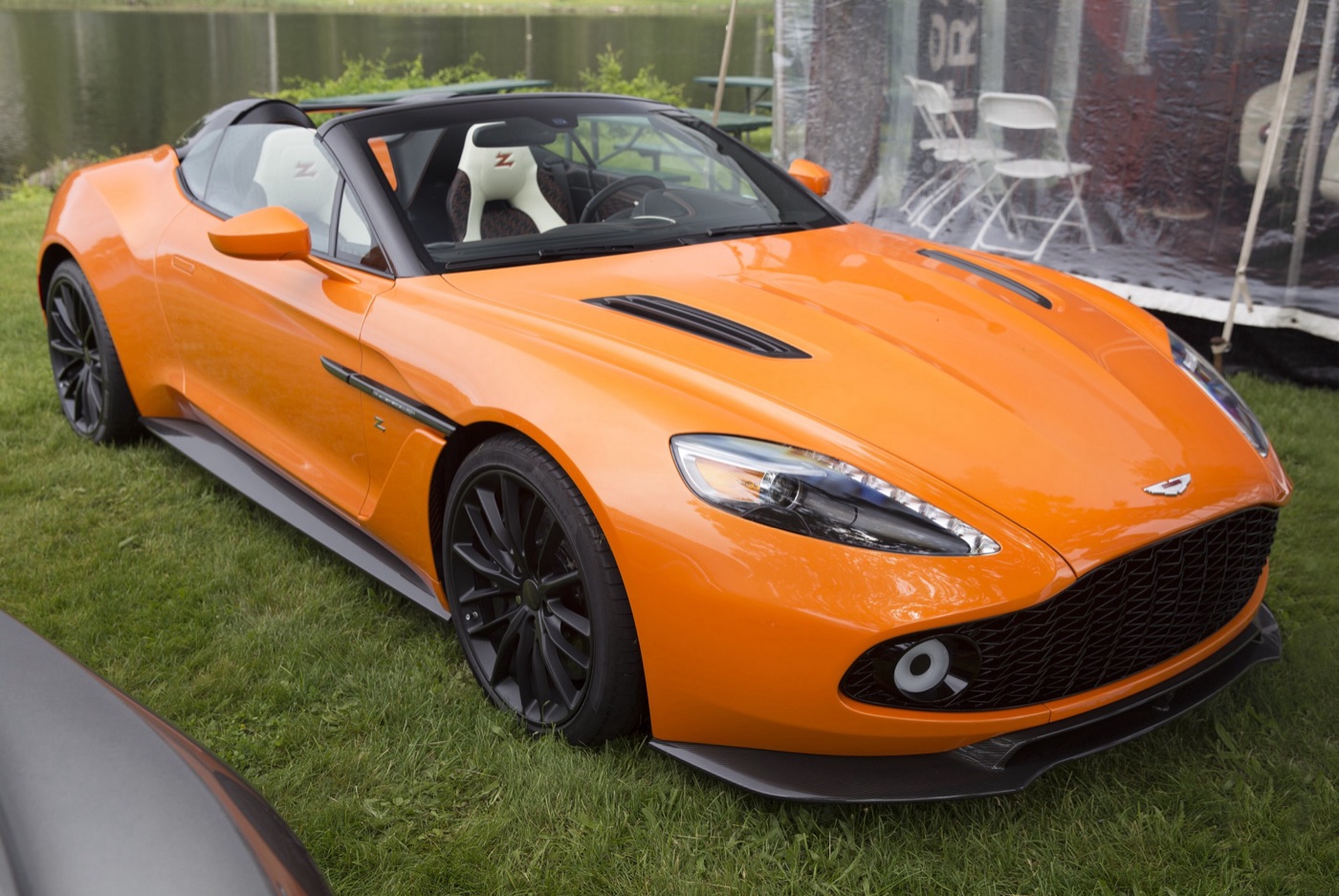 Orange Aston Martin Vanquish Zagato Speedster with two humps behind the seats and white leather seats, on a lawn