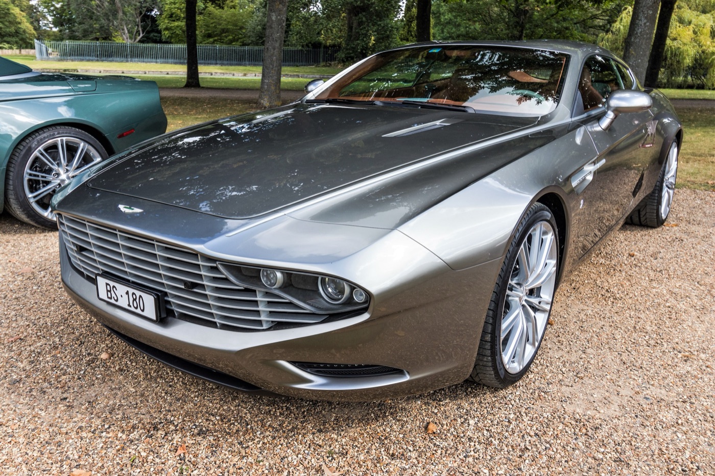 Grey Aston Martin Virage Shooting Brake Zagato with a wide slatted grille and a long estate roof, on gravel among trees