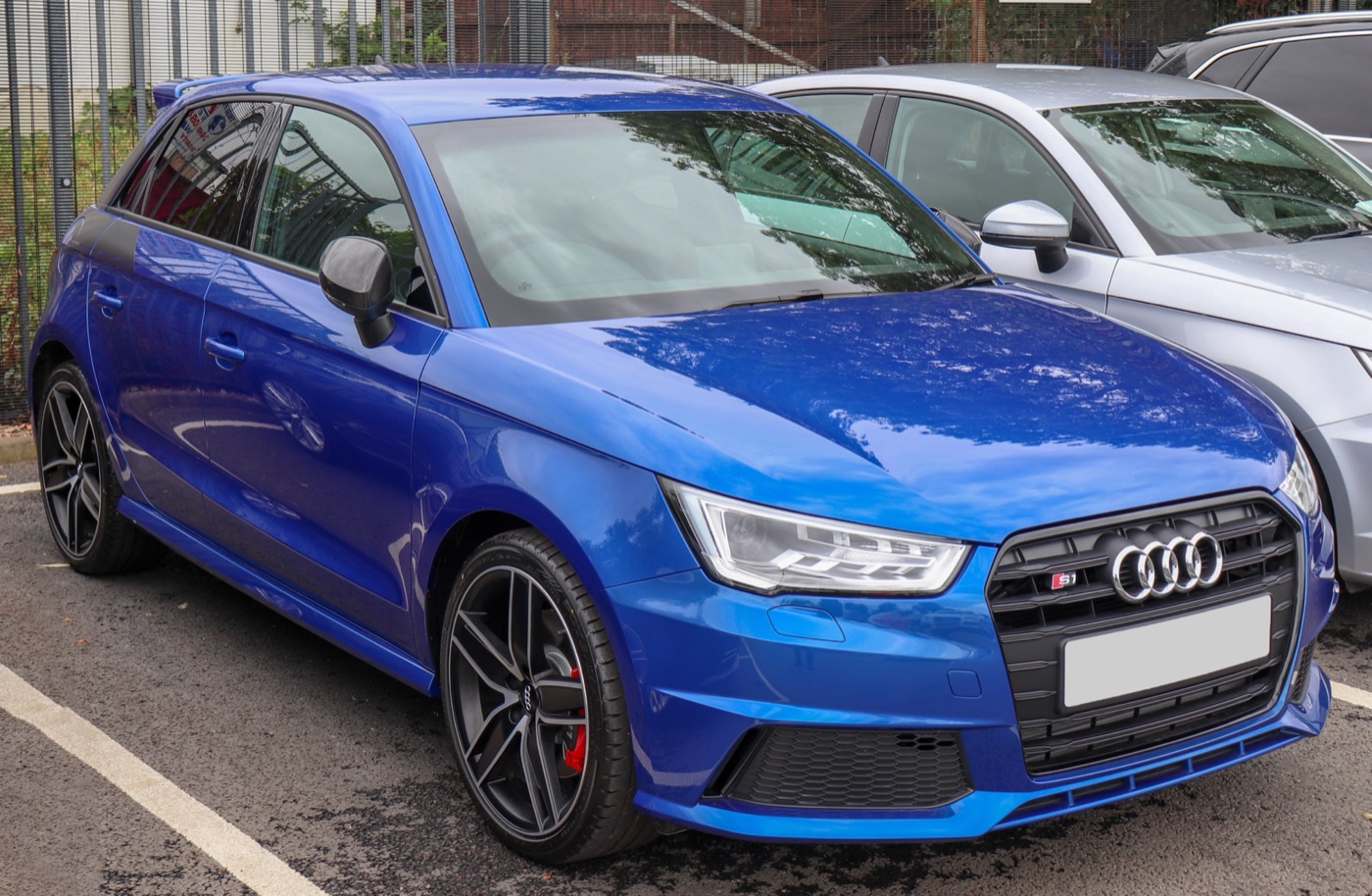 Blue Audi S1 Sportback with black wheels and red brake calipers in a car park