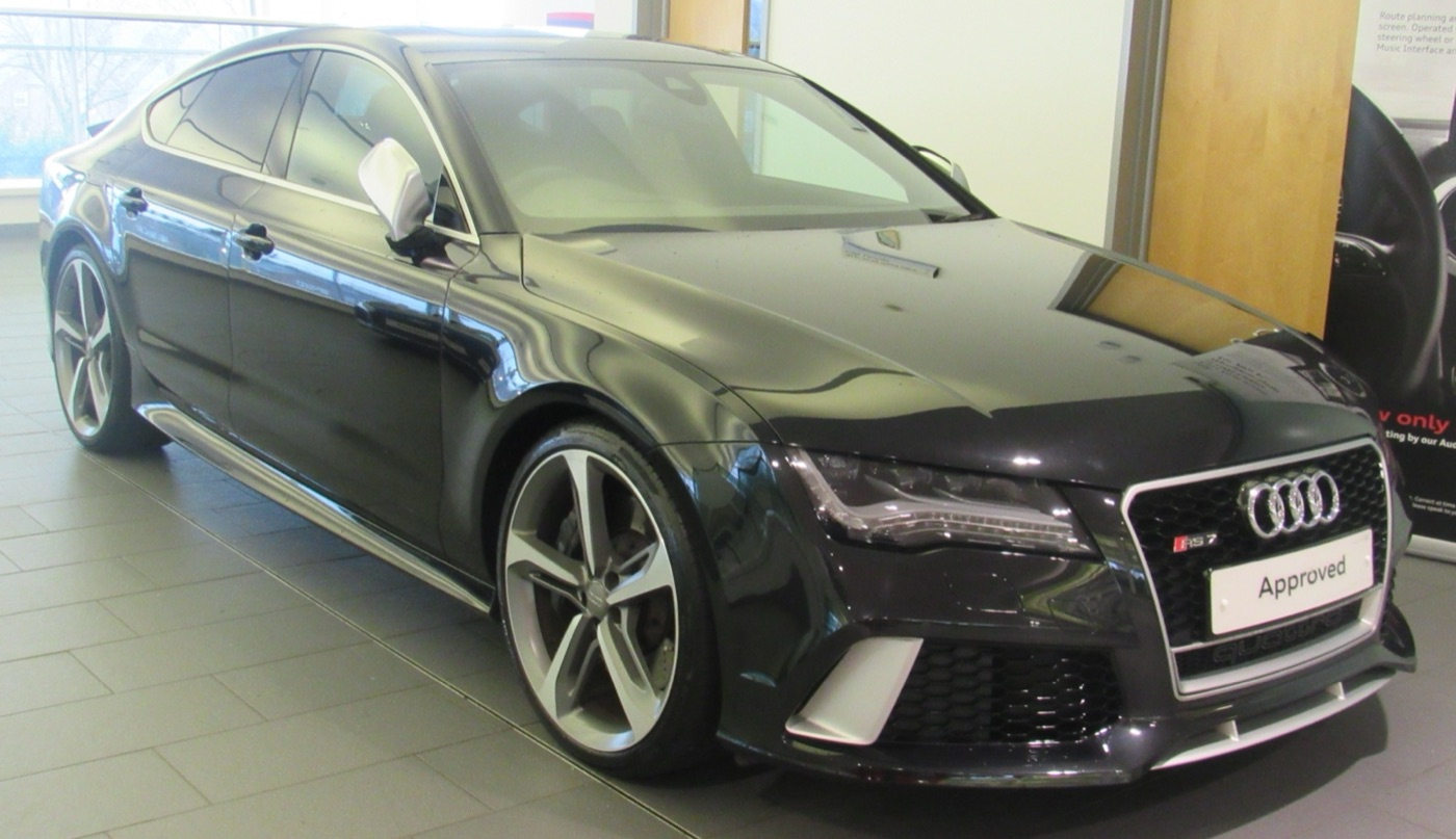 Black Audi RS 7 Sportback with gloss black honeycomb grille in a showroom, front three-quarter view