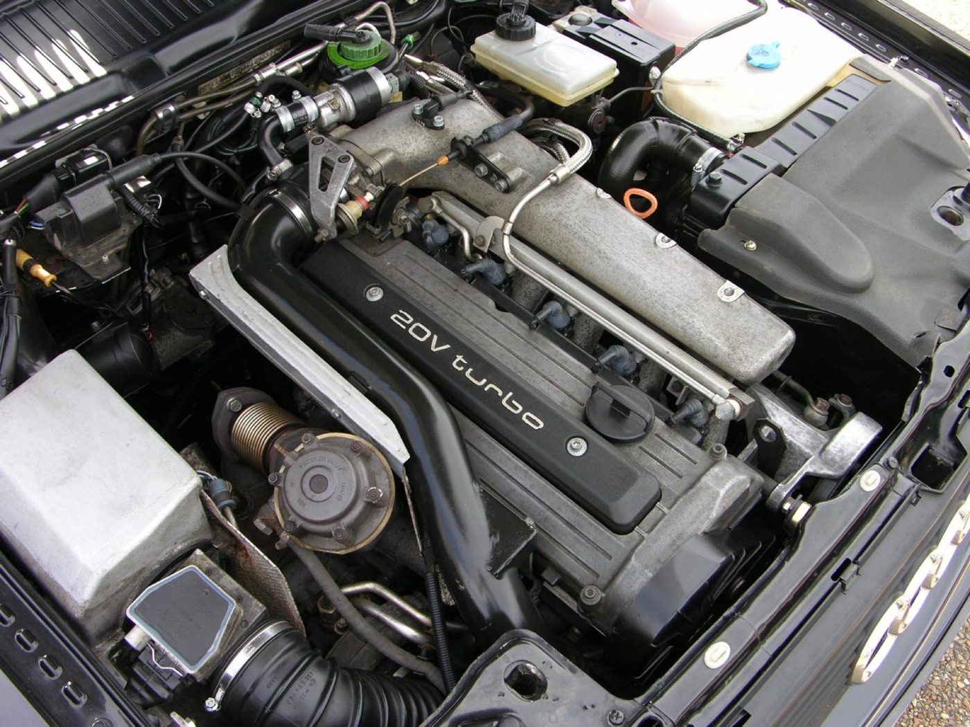 Engine bay of an Audi Quattro 20V with the five-cylinder engine’s black cam cover marked 20V turbo and the intake pipework