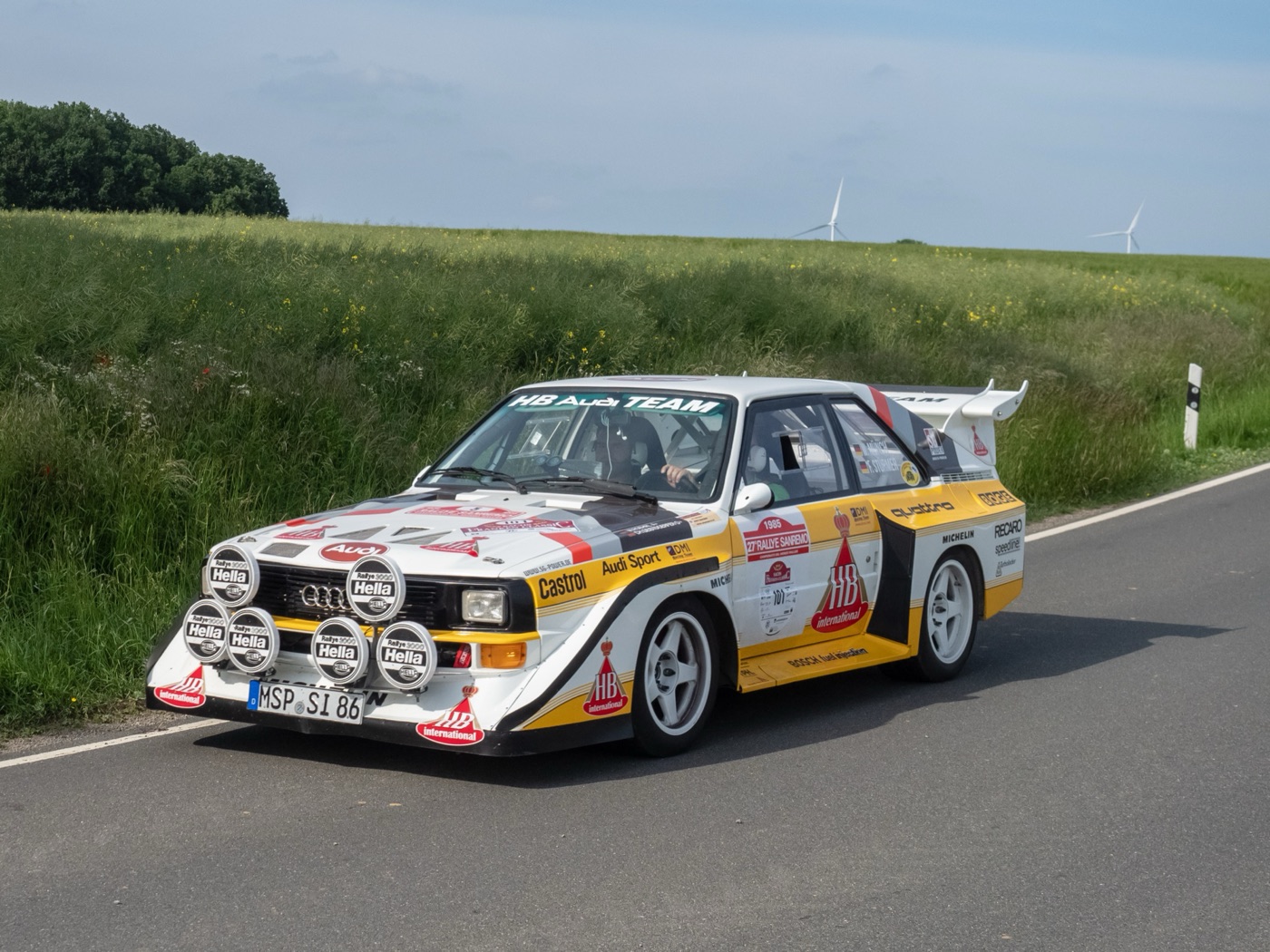 White and yellow HB Audi Team Sport quattro S1 E2 with a large rear wing and six Hella lamps on a country road