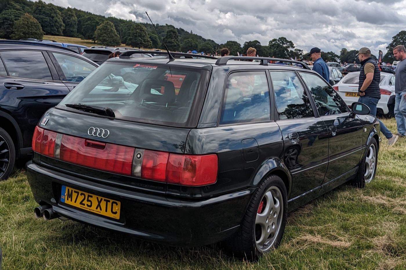 Rear view of a black Audi RS2 with the full-width red light strip, twin exhaust pipes and a British number plate, parked on grass