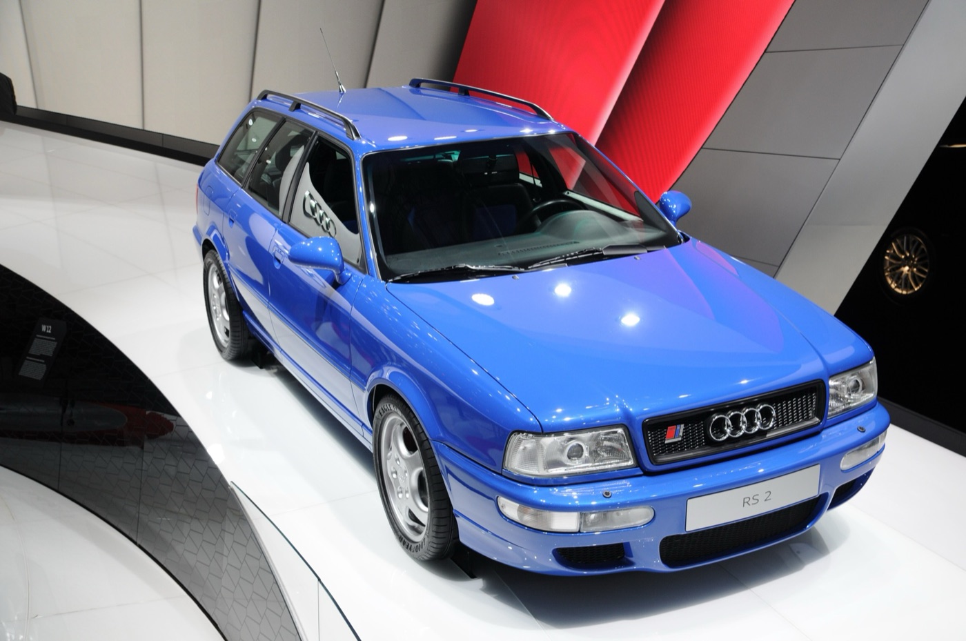 Nogaro blue Audi RS2 with a sign reading RS 2 on a white turntable under red and grey walls