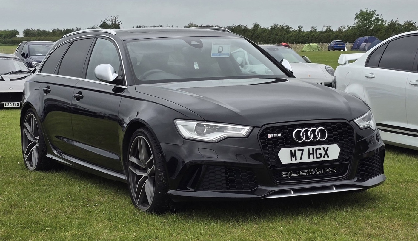Black pre-facelift Audi RS6 C7 Avant with quattro lettering in the front bumper, parked on grass among other cars