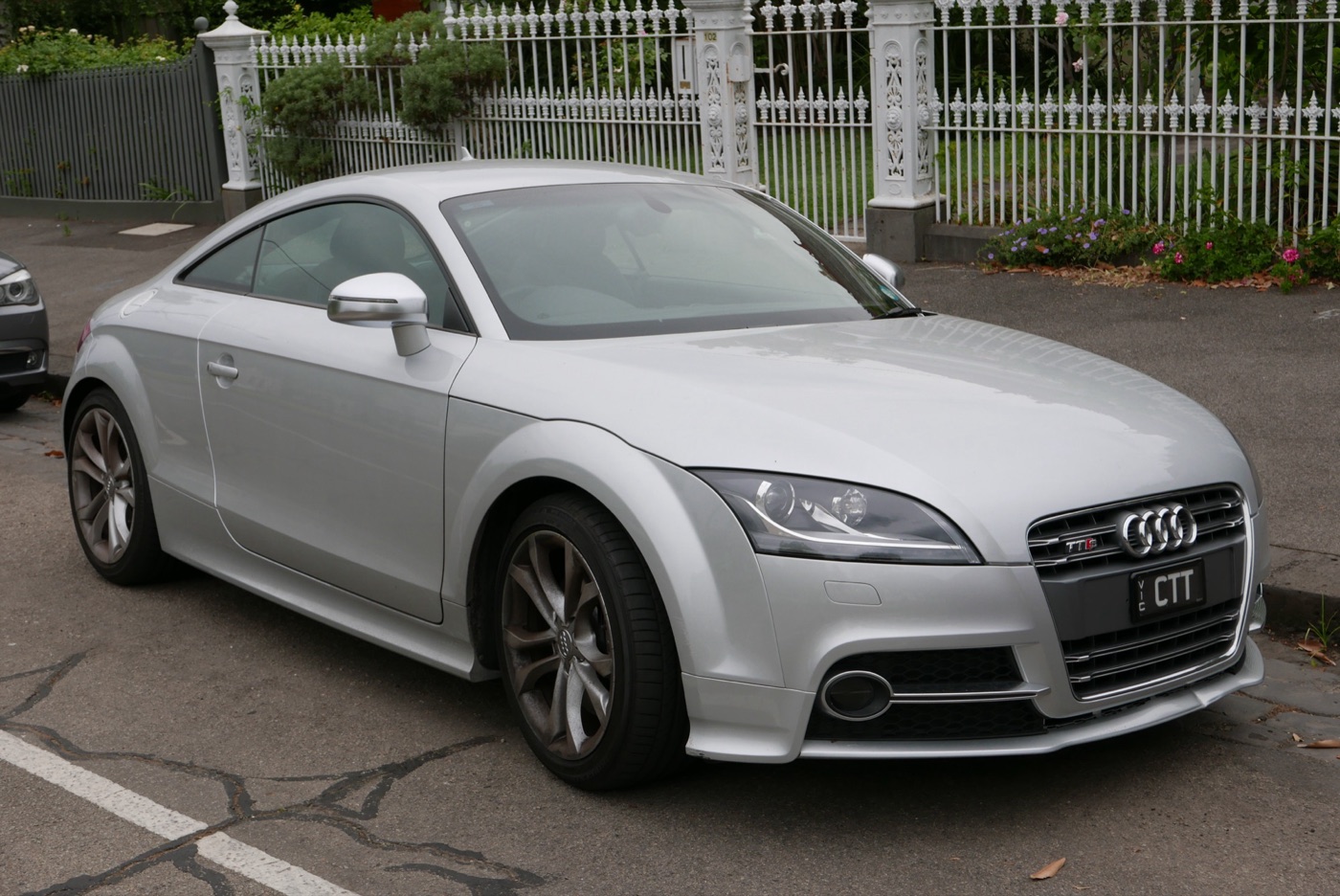 Silver facelifted Audi TTS coupe with a TTS grille badge parked by an iron fence