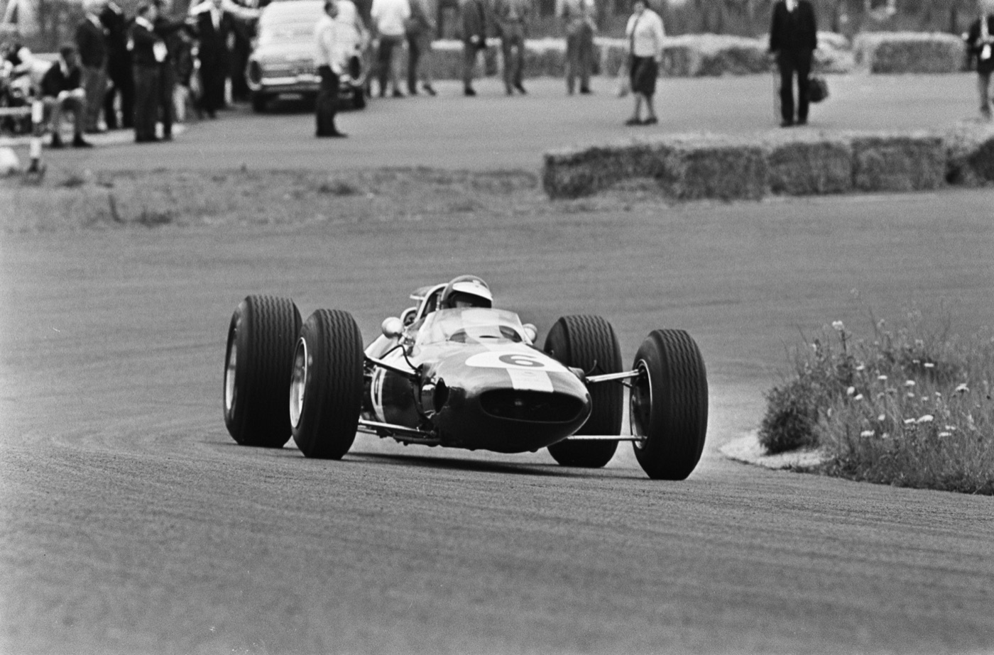 Black and white photograph of Jim Clark’s Lotus, number 6, cornering towards the camera at Zandvoort with spectators behind straw bales