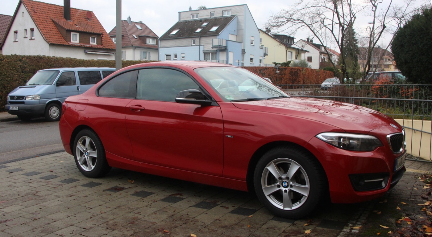 Red BMW 2 Series F22 Coupé with silver alloy wheels parked on cobbles in a German residential street