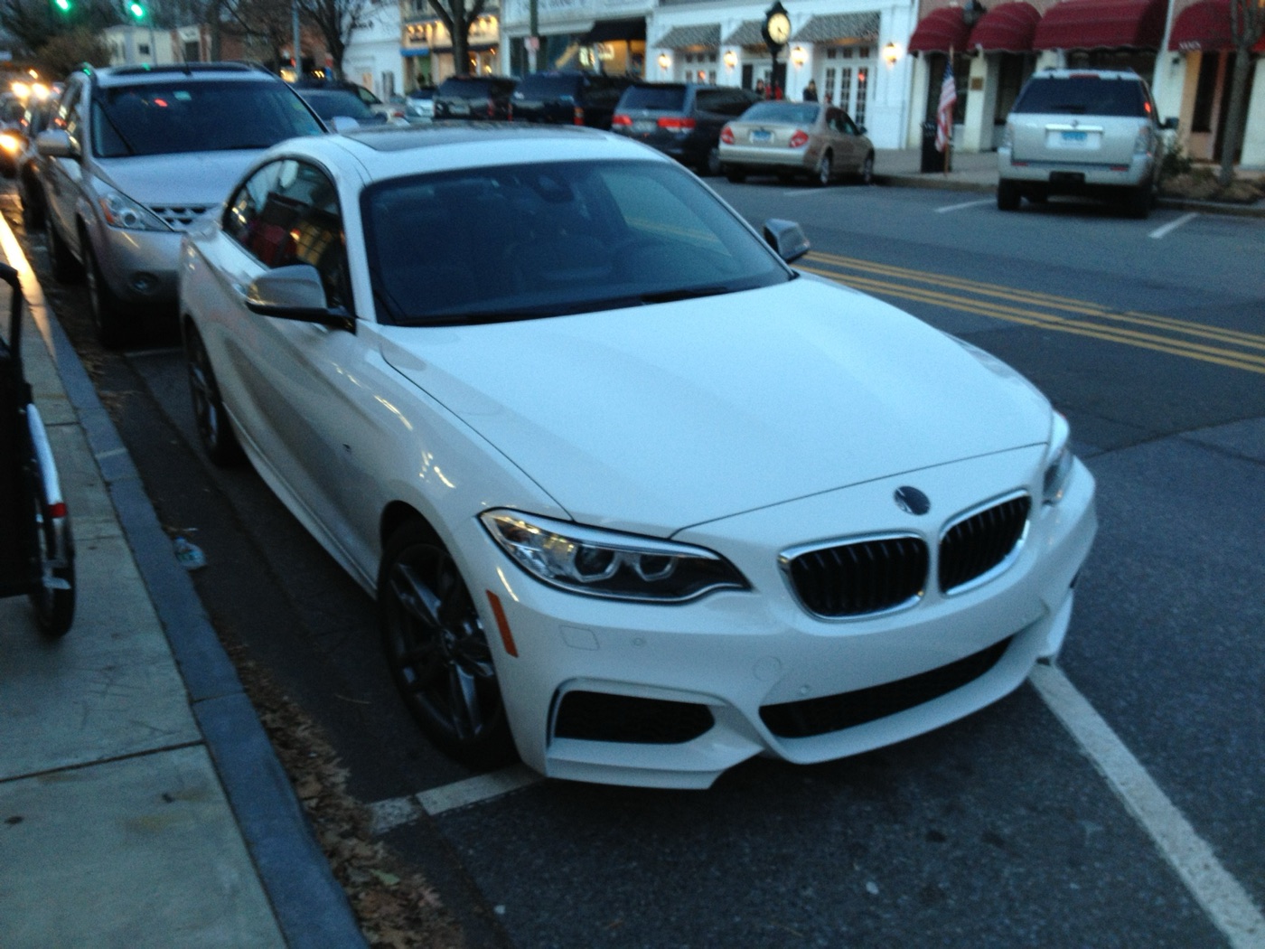 White BMW M235i coupé parked at a kerb in a small American town at dusk
