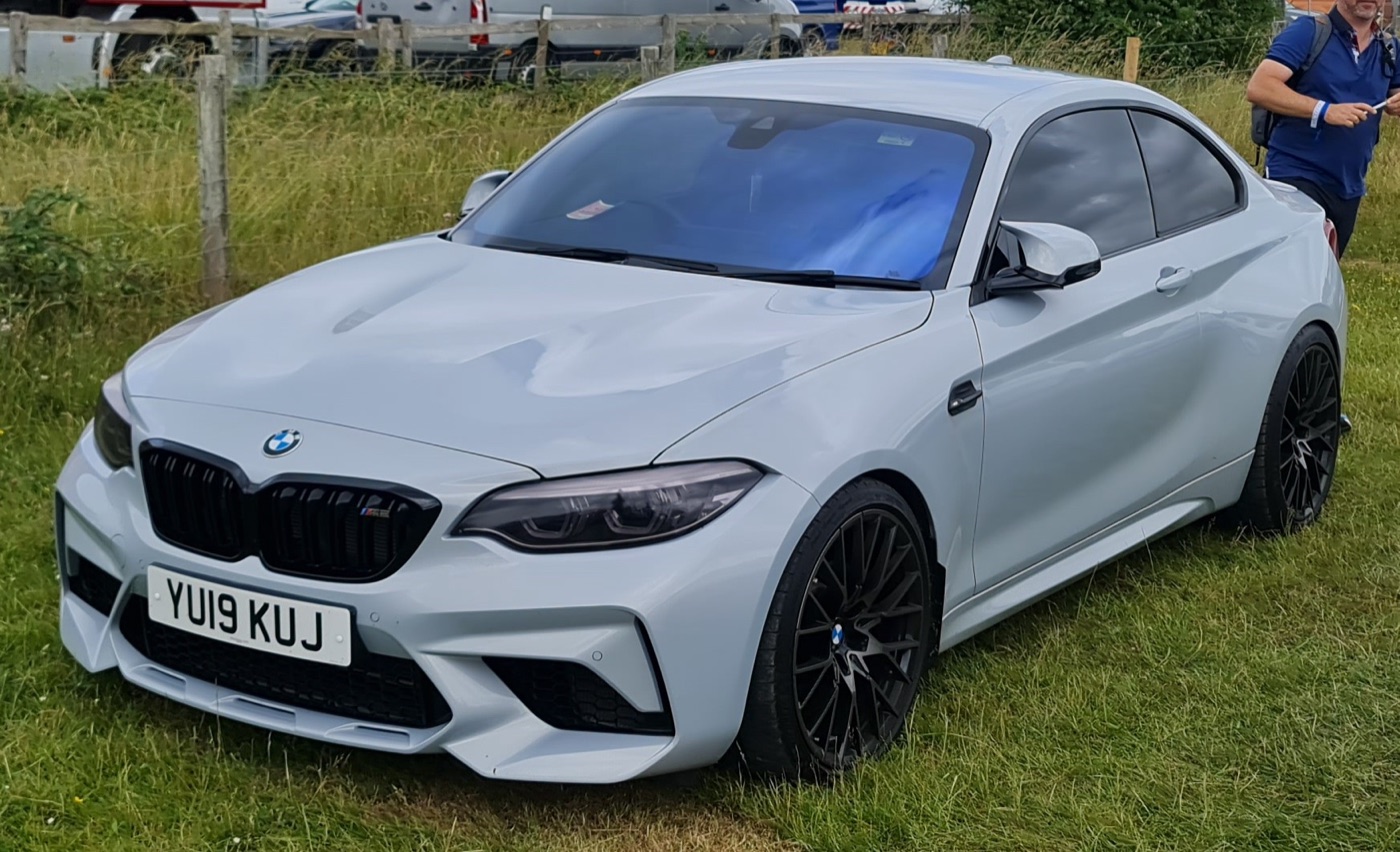 Pale grey BMW M2 Competition with black wheels and a British number plate parked on grass