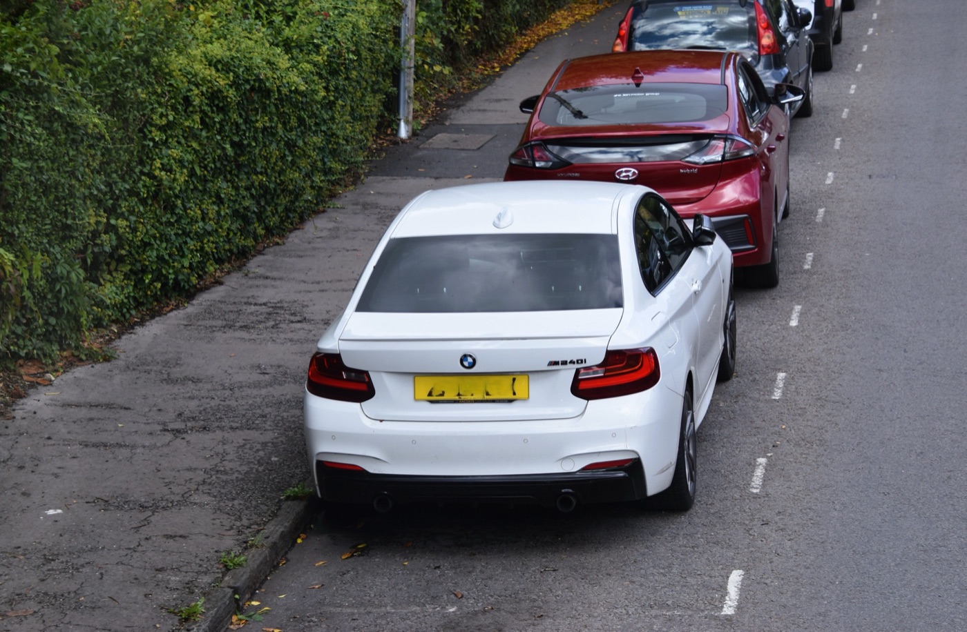 Rear of a white BMW M240i coupé with twin exhausts and an M240i badge on the boot lid, parked in a street