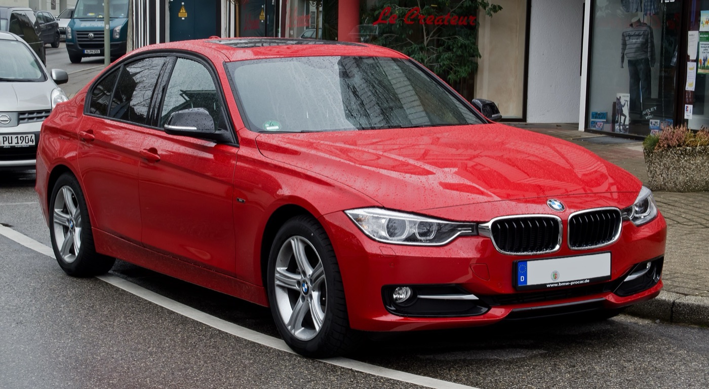 Red BMW 320d Sport Line F30 saloon with dealer plates parked on a wet town street