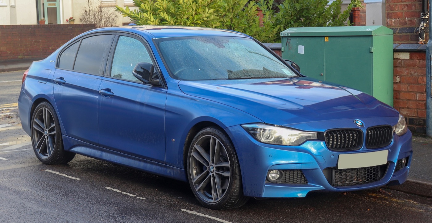Blue BMW 330e M Sport Shadow Edition saloon with black grille and dark alloy wheels parked beside a brick wall