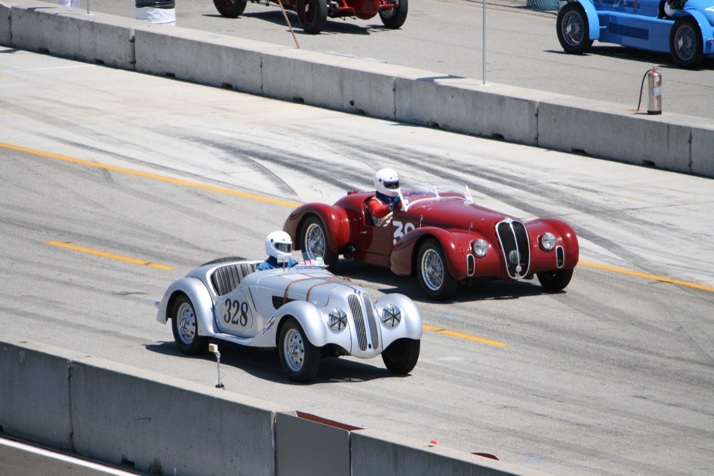 Silver BMW 328 roadster with race number 328 beside a red Alfa Romeo 6C 2500 Super Sport on a race circuit