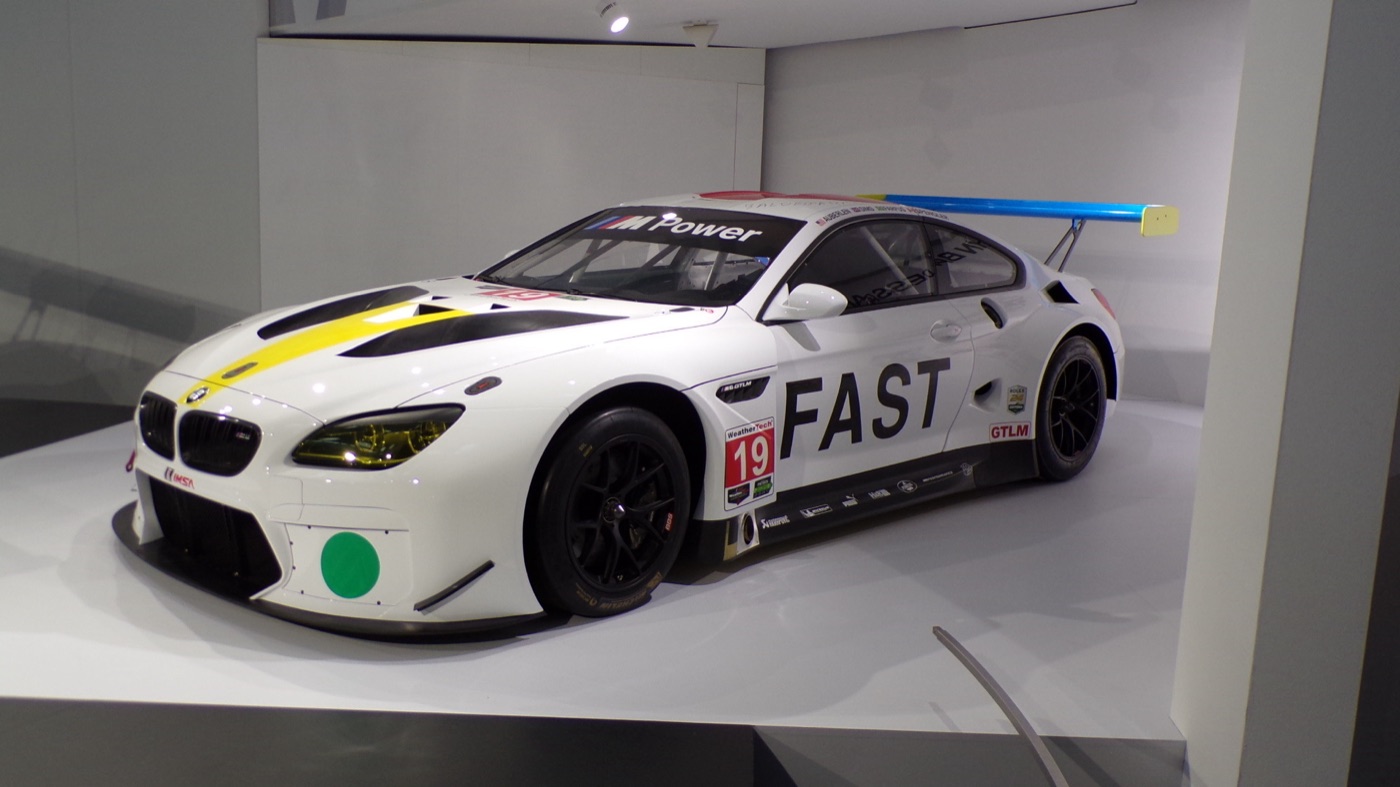 White BMW M6 GTLM Art Car by John Baldessari with the word FAST on its side, a green dot on the nose, race number 19 and a blue rear wing